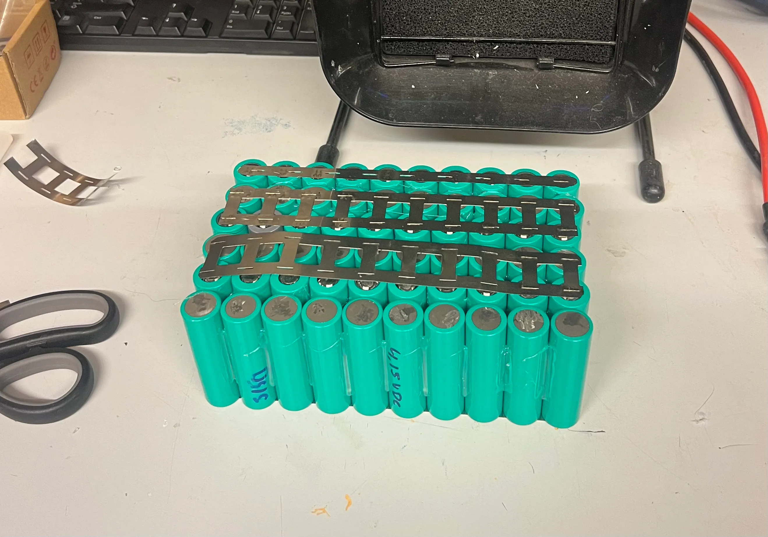 Bare Samsung 18650 cells arranged in a block on the workbench with nickel strips laid over them, before welding